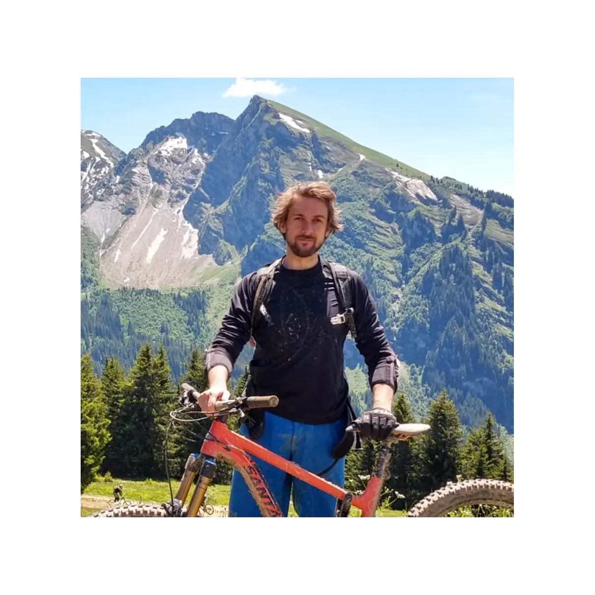Photo of Alex dressed for cycling and standing with a mountain bike in the French Alps